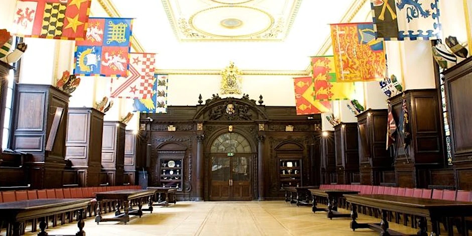 The hall of a livery company, showing flags on poles hung on both sides of a panelled room.